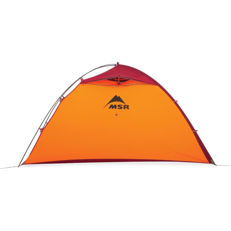 La carpa MSR Hubba Hubba 2 (copia), en naranja y rojo, se destaca sobre un fondo blanco que muestra su forma de cúpula y su diseño robusto con una estructura de postes de soporte visible. El icónico logotipo de MSR se muestra claramente en el lateral.