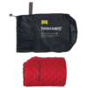 Una colchoneta hinchable Colchoneta Therm-a-Rest ProLite Plus roja, parcialmente desenrollada, se encuentra junto a su bolsa de almacenamiento negra. La bolsa abierta revela el nombre de la marca y los detalles del producto en texto blanco, lo que enfatiza la comodidad confiable de la colchoneta.