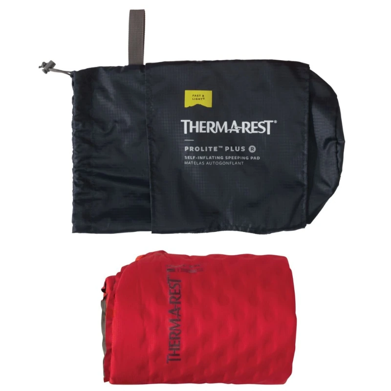 Una colchoneta hinchable Colchoneta Therm-a-Rest ProLite Plus roja, parcialmente desenrollada, se encuentra junto a su bolsa de almacenamiento negra. La bolsa abierta revela el nombre de la marca y los detalles del producto en texto blanco, lo que enfatiza la comodidad confiable de la colchoneta.
