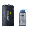 Una colchoneta para dormir compacta y de color gris oscuro, modelo Therm-a-Rest ProLite Plus, en una bolsa con cordón, se encuentra junto a una botella de agua Nalgene transparente con tapa azul, marcada con medidas de hasta 1000 ml.