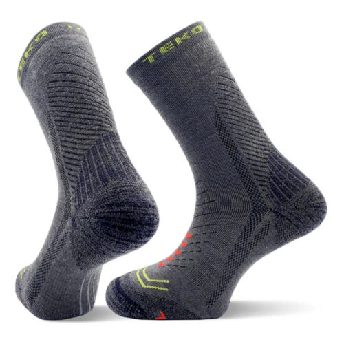 Un par de calcetines de senderismo Calcetín Teko EcoHike Discovery Light Half Cushion 2.0 de color gris oscuro, con patrones texturizados y detalles en verde neón y naranja, se mantienen en posición vertical, resaltando las secciones del talón y la puntera.
