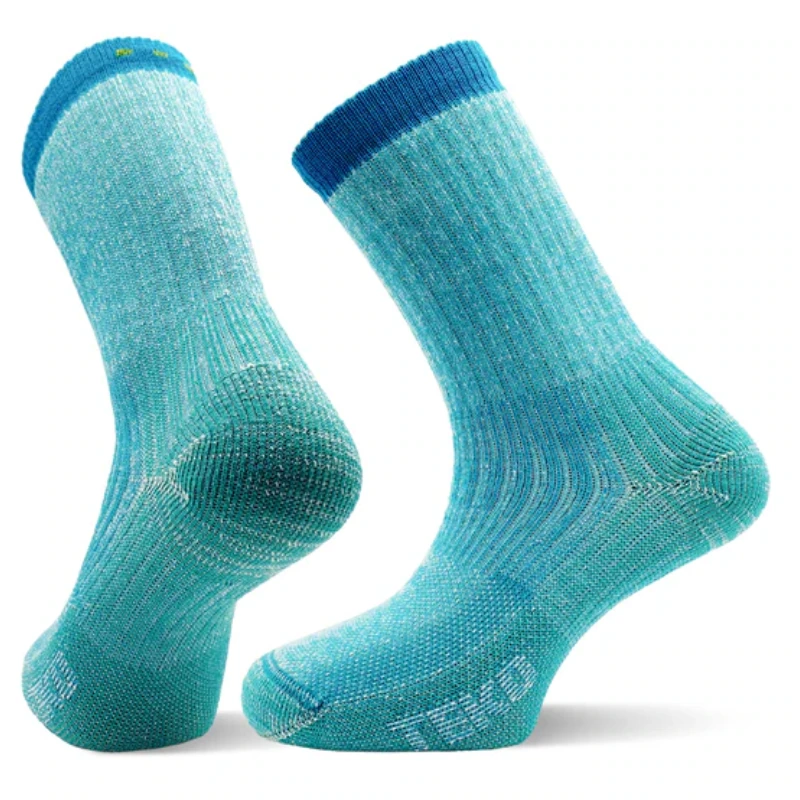 Se muestran dos calcetines Calcetín Teko EcoHikong Medium Full Cushion 3.0 en color azul verdoso. La parte inferior del calcetín izquierdo revela una amortiguación gruesa, mientras que el calcetín derecho se mantiene en posición vertical, mostrando su textura acanalada y su puño en azul más oscuro.