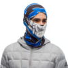 El individuo, que lleva un pasamontañas azul y negro con un diseño de calavera estilizada, se destaca con su Bandana Buff Original EcoStretch Licenses Valparaíso 2020 (copia). Vestido con una chaqueta acolchada gris claro sobre un fondo blanco liso, su apariencia es llamativa y audaz.