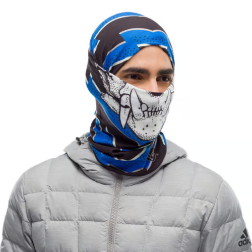 El individuo, que lleva un pasamontañas azul y negro con un diseño de calavera estilizada, se destaca con su Bandana Buff Original EcoStretch Licenses Valparaíso 2020 (copia). Vestido con una chaqueta acolchada gris claro sobre un fondo blanco liso, su apariencia es llamativa y audaz.