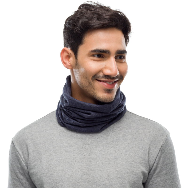 Un hombre con cabello oscuro y barba sonríe mientras usa la Bandana Buff Merino Midweight Night Blue Melange y una sudadera gris claro sobre un fondo blanco.