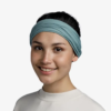 Una persona alegre, que viste un pañuelo azul y una camisa blanca impecable, se encuentra de pie frente a un fondo blanco liso.