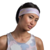 Una persona con una diadema y una camiseta sin mangas de color pastel se encuentra de pie frente a un fondo blanco, mirando hacia adelante de manera neutral, con sus Cinta Buff CoolNet UV Slim Ahin Azure (copia) que le aportan una elegancia vibrante.