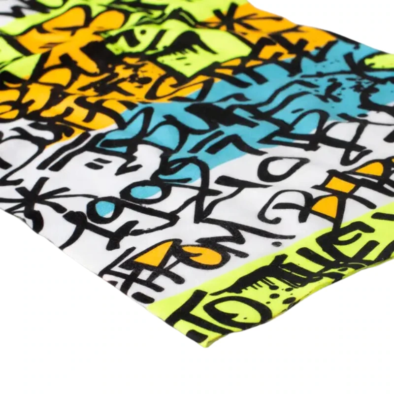 Un primer plano de una tela con un diseño vibrante estilo graffiti como el Bandana Buff Original EcoStretch Grafft 2.0 Multi, que presenta letras y formas abstractas en negro sobre un fondo azul, amarillo y verde brillante para una apariencia urbana dinámica que es elegante y ecológica.