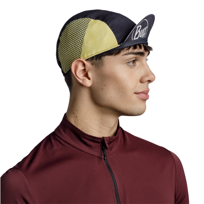 Un hombre con una camiseta de color granate con cremallera lleva la gorra Jockey Buff Pack Cycle Lenir Night Blue, caracterizada por un estampado negro y amarillo con paneles de malla. El logotipo añade un toque deportivo mientras mira hacia la derecha sobre un fondo blanco sencillo, lo que resalta su aspecto moderno y activo.