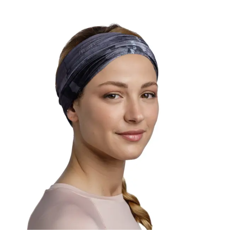 Una persona con expresión tranquila, que lleva una banda para el pelo Bandana Buff Original EcoStretch Neski Multi y una camiseta de color claro, tiene el pelo recogido en una trenza sobre un hombro. El fondo es blanco liso.