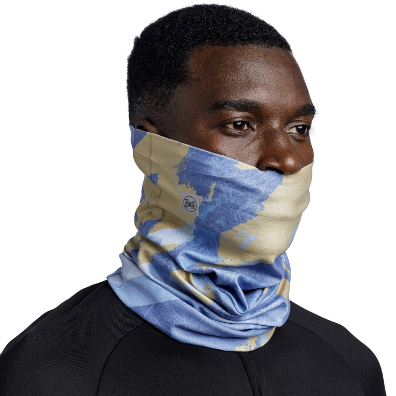 Una persona lleva una polaina para el cuello Bandana Buff ThermoNet Surib Multi que le cubre la nariz y la boca. Lleva una camiseta negra y la polaina tiene el logotipo de la marca con un patrón similar al estilo Buff Original sobre un fondo blanco liso.