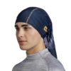 Una persona con cabello castaño corto lleva una camiseta Buff Original EcoStretch Moulay Night Blue larga, parecida a un pañuelo, con una pequeña etiqueta con el logotipo de color naranja y texto vertical. Su camisa de cuello alto de color gris claro complementa el look mientras mira ligeramente hacia un lado con una expresión neutra.