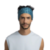 Un hombre de pelo corto y oscuro y barba recortada lleva una cinta para la cabeza Cinta Buff CoolNet UV Wide Ater Teal con un estampado de camuflaje. Lleva una camiseta sin mangas de color azul claro sobre un fondo blanco liso.