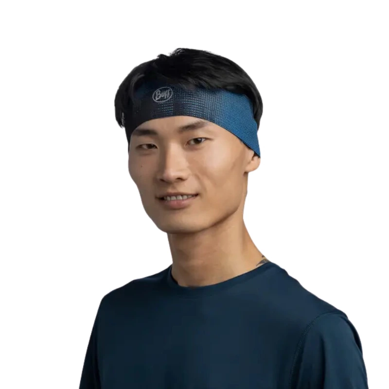 Una persona que lleva una diadema Cinta Buff CoolNet UV Slim Tasie Multi y una camisa azul oscuro sonríe a la cámara sobre un fondo blanco liso.