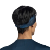 Se muestra a una persona de espaldas con el pelo corto y negro, que lleva una cinta para la cabeza Cinta Buff CoolNet UV Slim Tasie Multi. También lleva una camiseta azul oscuro y está de pie sobre un fondo blanco liso.