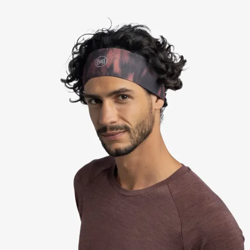 Una persona con cabello rizado que lleva una diadema Cinta Buff CoolNet UV Slim Sishpink Fluor y una camisa granate posa sobre un fondo blanco liso.