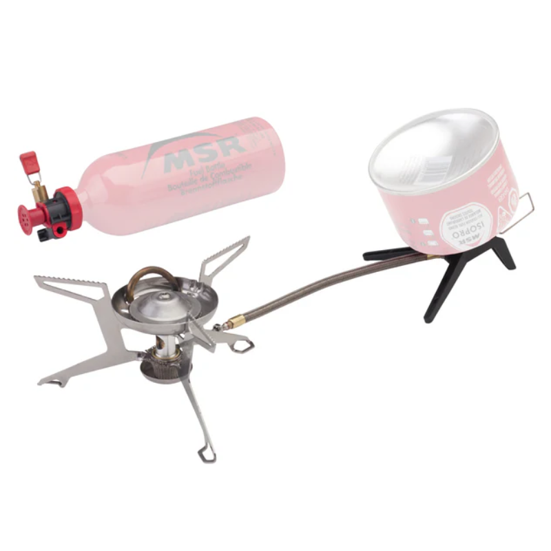 Una estufa de camping portátil configurada con Cocinilla MSR WhisperLite Universal incluye una botella de combustible roja unida a una estufa plateada con un trípode, junto con una olla pequeña colocada sobre un soporte negro para cocinar.