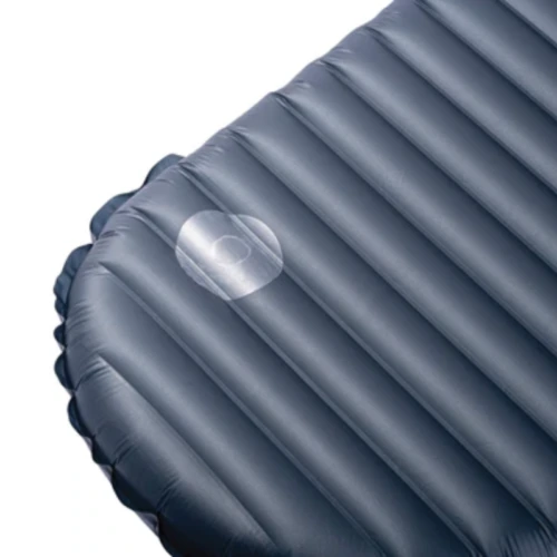 Un primer plano de un colchón inflable gris, similar al Tensores Reflectantes MSR Reflective Utility Cord (copia), muestra una reparación con un parche circular cerca del centro. La textura acanalada se destaca claramente contra el fondo blanco liso.