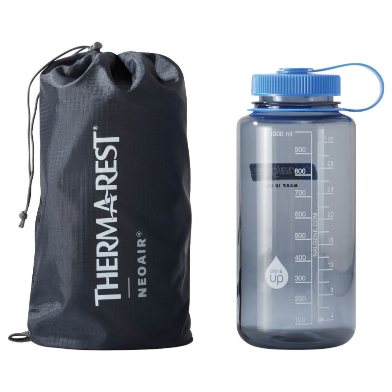 Una bolsa con cordón de color azul oscuro con la inscripción "Colchoneta Therm-a-Rest NeoAir XLite NXT (copia)" en blanco se encuentra junto a una botella de agua transparente de 1000 ml con tapa de rosca azul y marcas de medición.