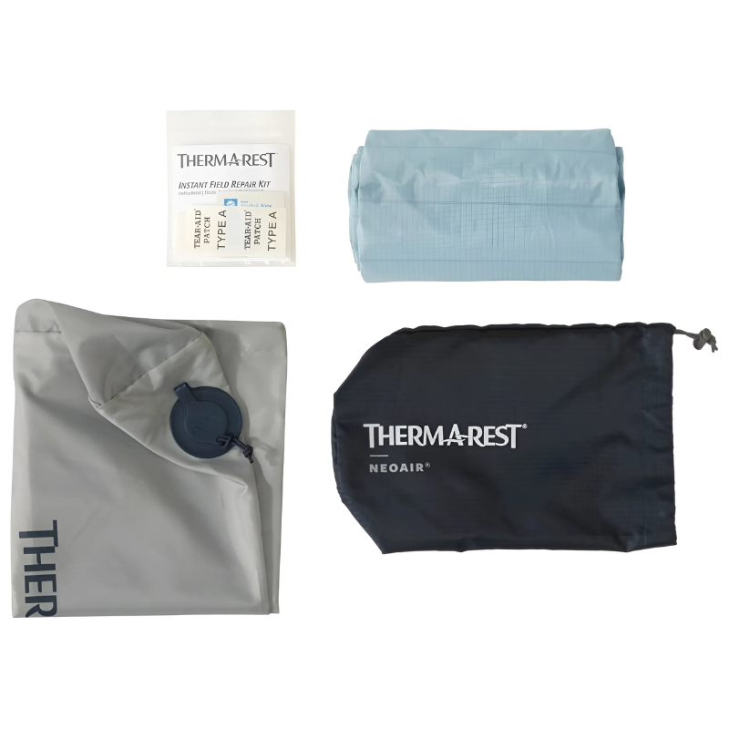 Una colchoneta enrollada de color azul, una bolsa inflable de color gris, una bolsa de almacenamiento ThermaRest NeoAir de color negro y un pequeño kit de reparación instantánea en el campo (que incluye la avanzada Colchoneta Therm-a-Rest NeoAir XTherm NXT) están dispuestos sobre un fondo blanco.