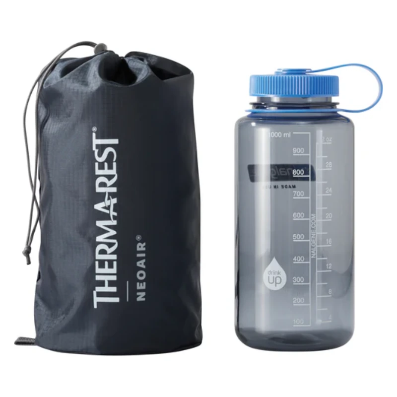 Una bolsa Colchoneta Therm-a-Rest NeoAir XTherm NXT MAX (copia) negra con cordón se encuentra junto a una botella de agua transparente de 1000 ml con una tapa azul, marcas de medición y un asa azul adjunta.