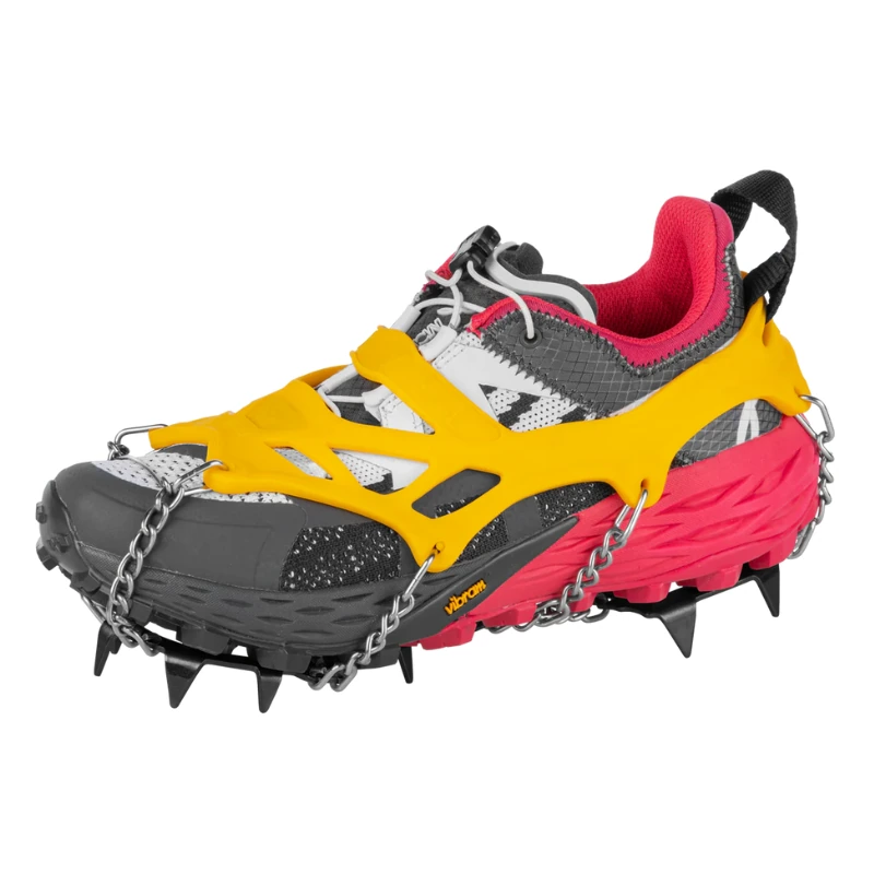 Una zapatilla de trail gris/roja con un dispositivo de tracción amarillo/negro, con clavos y cadenas de metal para un agarre excepcional en hielo o nieve, similar al agarre confiable de los Guantes Grivel Rock en subidas desafiantes.