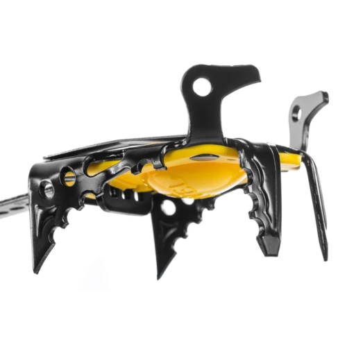 Primer plano de un crampón de escalada de metal negro con puntas afiladas. Los crampones de alpinismo Técnico Grivel G22 Plus (copia) cuentan con una base amarilla para la fijación de la bota, lo que garantiza la tracción en hielo y nieve. La imagen se centra en la vista lateral de estos crampones.