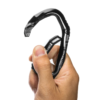 Una mano sostiene un Mosquetón Grivel Stealth, con el pulgar y el índice presionando el gatillo. El mosquetón está abierto, resaltando su diseño curvo y su construcción en metal.