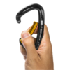 Una mano sosteniendo un elegante Mosquetón Grivel K1 negro y amarillo sobre un fondo blanco prístino.