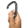 Una mano sostiene un mosquetón Grivel K3EW Plume Evo Wire, presionando la compuerta para abrirla con el pulgar y el índice contra un fondo blanco liso.
