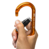 Una mano sostiene un Mosquetón Grivel K18T Wide Twist-Lock naranja con mecanismo negro, listo para enganchar el mosquetón metálico curvo y resistente sobre un fondo blanco liso.