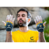 Un hombre que lleva una camiseta amarilla con el logo de "Grivel" se encuentra al aire libre, con las manos cubiertas de tiza. Lleva guantes Grivel Rock Gloves (copia) en amarillo y negro, y parece concentrarse contra el fondo rocoso y accidentado.