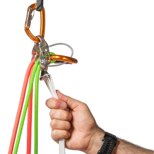Una persona con un reloj de pulsera negro sujeta una cuerda de escalada blanca a través de un dispositivo de aseguramiento Grivel Master (copia). Está unida a mosquetones de color naranja, mientras que cuerdas rojas, verdes y rayadas cuelgan hacia abajo sobre un fondo blanco liso.