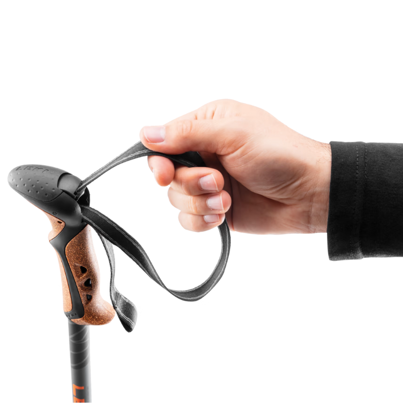 Una mano agarra el mango de unos Bastones de Trekking Leki Lhasa Mujer (copia) con una correa ajustable de color negro, con empuñadura de corcho y elegantes detalles de plástico negro sobre un fondo blanco liso.