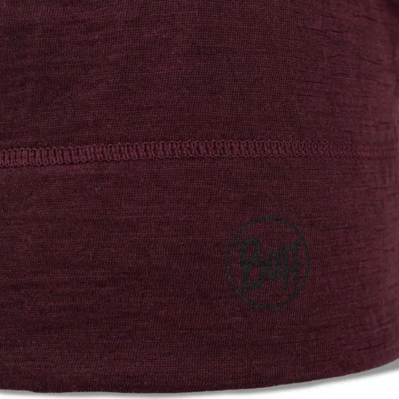 Un primer plano de una tela marrón con una línea de costura horizontal muestra la artesanía del Gorro Buff Lightweight Beanie, que presenta un sutil logotipo circular con "Buff" en la esquina inferior derecha.
