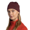 Una persona con cabello largo lleva una diadema roja y una chaqueta roja con cremallera, imitando el elegante estilo de un gorro ligero Gorro Buff. Mantiene una expresión neutra, mirando ligeramente hacia un lado sobre un fondo blanco liso.