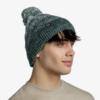 Una persona con cabello corto y oscuro lleva un gorro de lana gris y verde de la marca Gorro Buff Knitted y Polar Kim (copia), con un pompón, mientras mira hacia la derecha. Su expresión es neutra, combinada con un suéter beige sobre un fondo blanco liso.