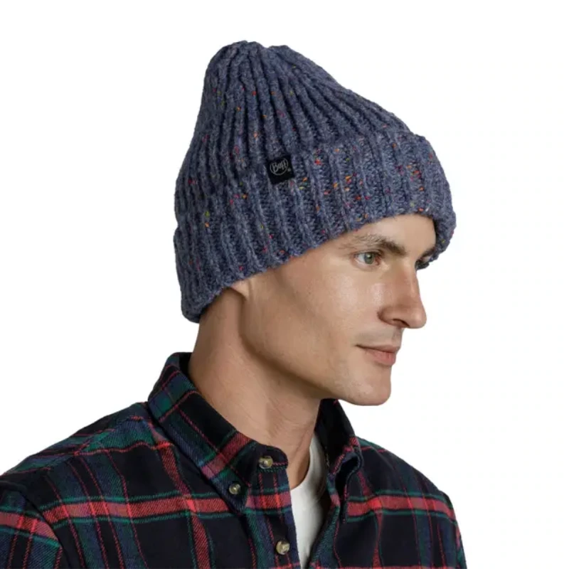 Una persona con una camisa a cuadros viste con estilo el Gorro Buff Knitted y Polar Caryn (copia), un gorro azul acanalado con motas de colores y una pequeña etiqueta con el logotipo en el lateral, mientras se muestra de perfil, mirando hacia la izquierda.