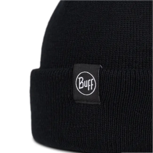 Primer plano de un gorro de punto negro, que recuerda al estilo Fisherman de Lilon, con una pequeña etiqueta rectangular con la palabra "Buff" en letras blancas dentro de un círculo. El fondo blanco liso resalta la textura del gorro.
