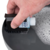 Una mano usa un cepillo pequeño para aplicar el jabón "Wilderness Wash" sobre una superficie oscura con agua espumosa. Cerca de allí, una paleta de bolsillo de nailon 66 Sea to Summit de Pala Plegable (copia) está lista para cualquier aventura al aire libre.