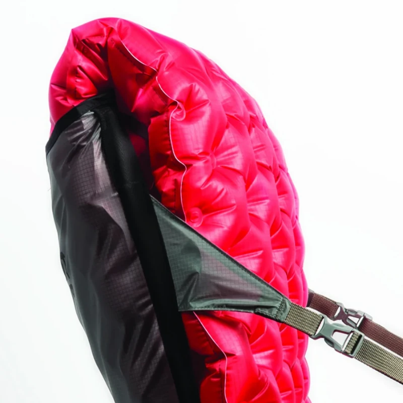 Primer plano de una colchoneta para dormir acolchada roja Sea to Summit Aeros Premium sujeta a una mochila negra con correas y hebillas, lo que resalta su diseño práctico. Una silla inflable Sea to Summit Air Chair complementa la escena sobre un fondo blanco nítido.