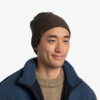 Una persona lleva un gorro Buff Niños Knitted y Polar Lyne y una chaqueta polar azul Polar Masha sobre un suéter beige sobre un fondo blanco liso.