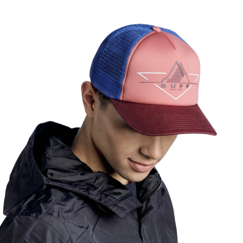 La persona lleva una gorra Jockey Buff Trucker Reth, con un logotipo geométrico en la visera granate, y la combina con una elegante chaqueta negra con capucha. Mira hacia abajo contra el fondo completamente blanco.