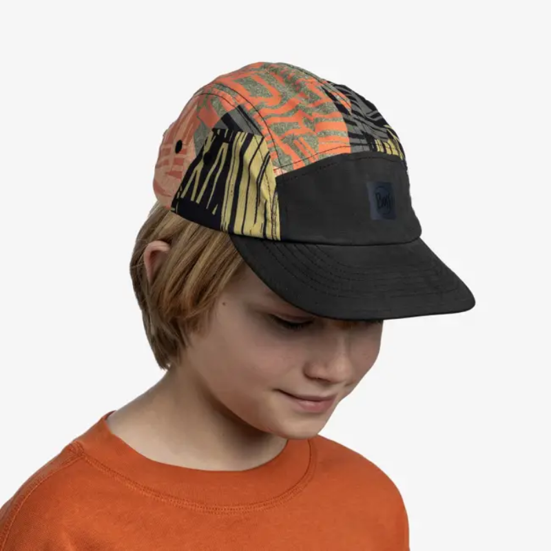 Un niño rubio, que viste una camiseta naranja y la colorida gorra Jockey Buff 5 Panel Go Pow Running Multi, mira hacia abajo sobre un fondo blanco liso.