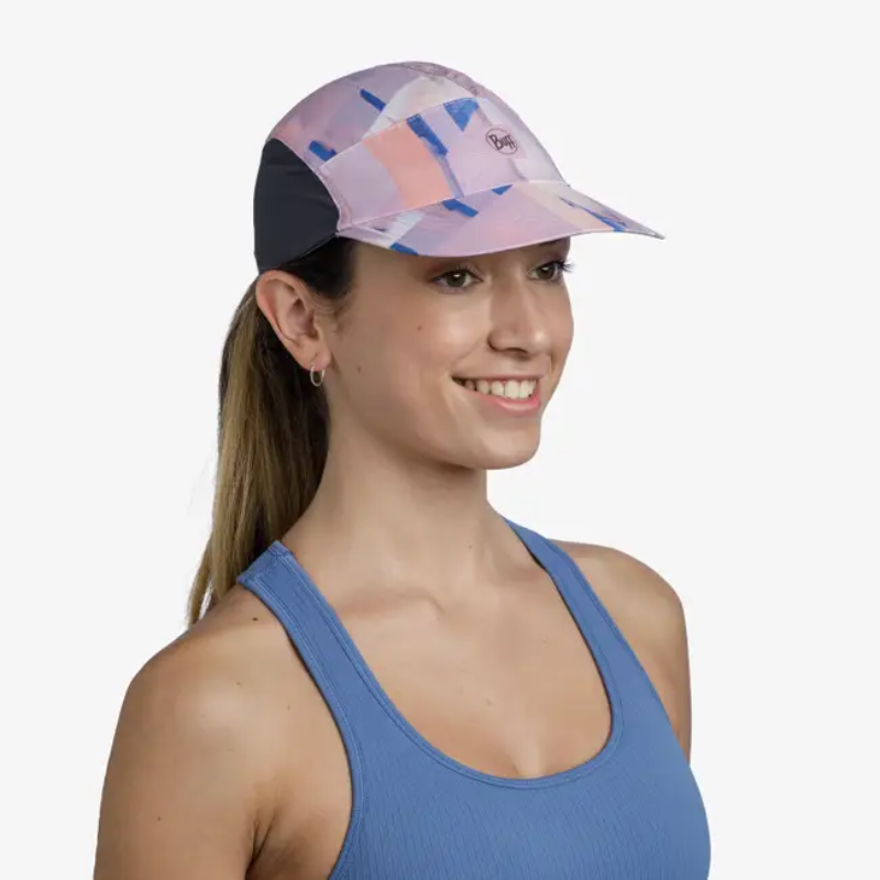 Sobre un fondo blanco liso, una mujer sonríe radiante mientras lleva una gorra "Jockey Buff Speed Pink Deri" con elegantes laterales negros. Lleva una camiseta azul sin mangas y el pelo recogido en una cola de caballo.