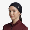 La persona lleva un pañuelo negro en la cabeza y una camiseta con cremallera color granate, y luce un look informal con la Cinta Buff CoolNet UV Slim Keffy Nectarine. Su leve sonrisa y expresión serena se destacan contra el fondo blanco liso.