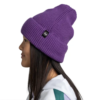 Una mujer con un gorro Buff Niños Knitted Beanie Rics morado (copia) mira hacia la izquierda, con cabello largo y oscuro, y vistiendo una chaqueta blanca y verde sobre un fondo blanco liso.