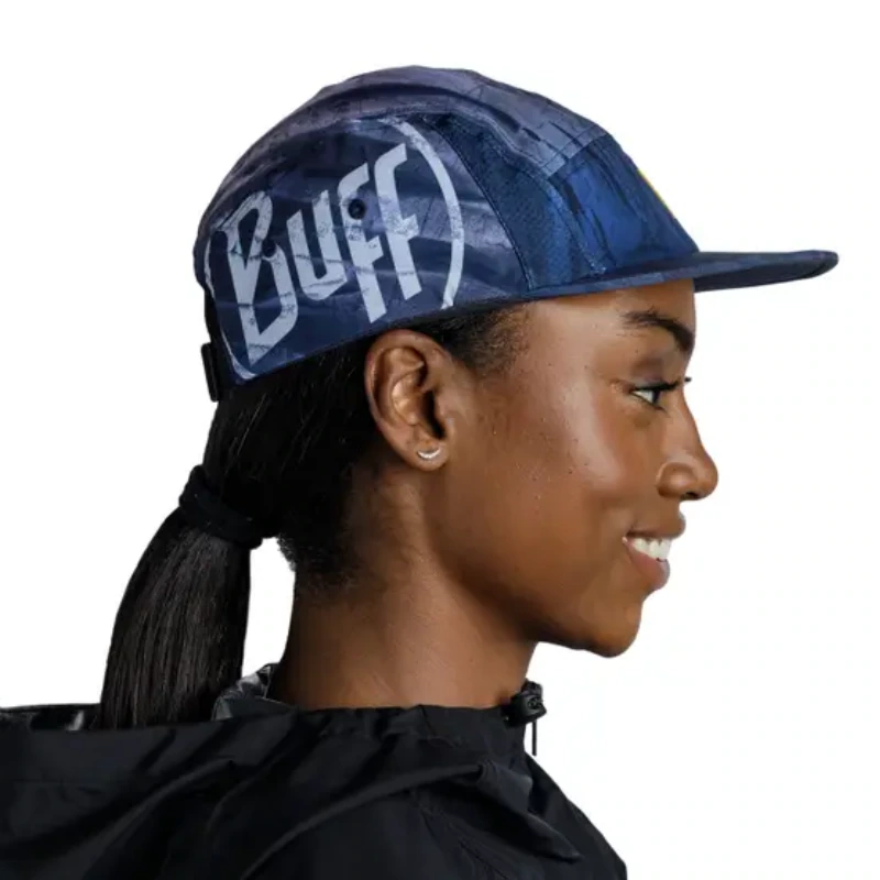 Una persona sonríe cálidamente con una gorra Jockey Buff Speed Pink Deri (copia) y una elegante chaqueta negra, con el pelo peinado sin esfuerzo en una cola de caballo baja. El fondo blanco liso realza su sencillez y encanto, y añade velocidad y gracia que recuerdan a un jockey.