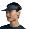 Se muestra a una persona de perfil con un Visera Buff Go Jaru Black, con una correa negra ajustable, que complementa elegantemente su camisa azul sobre un fondo blanco liso.