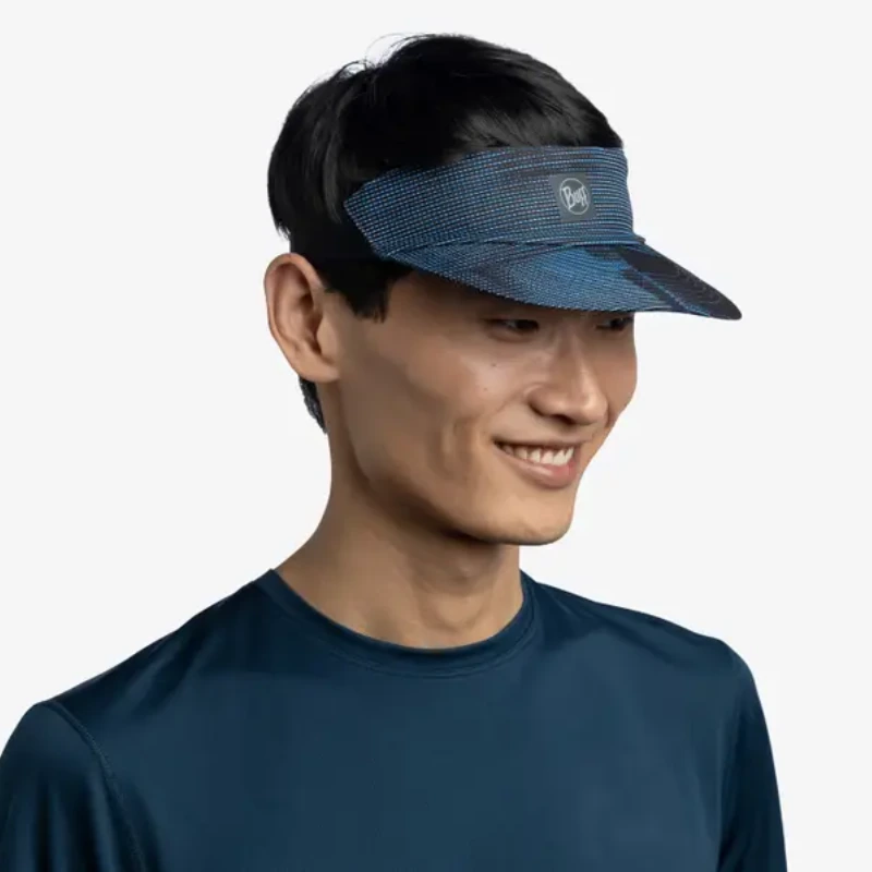 Una persona con cabello corto y oscuro sonríe, vistiendo una visera Visera Buff Go Jaru Black (copia) y una camisa azul oscuro sobre un fondo blanco liso.